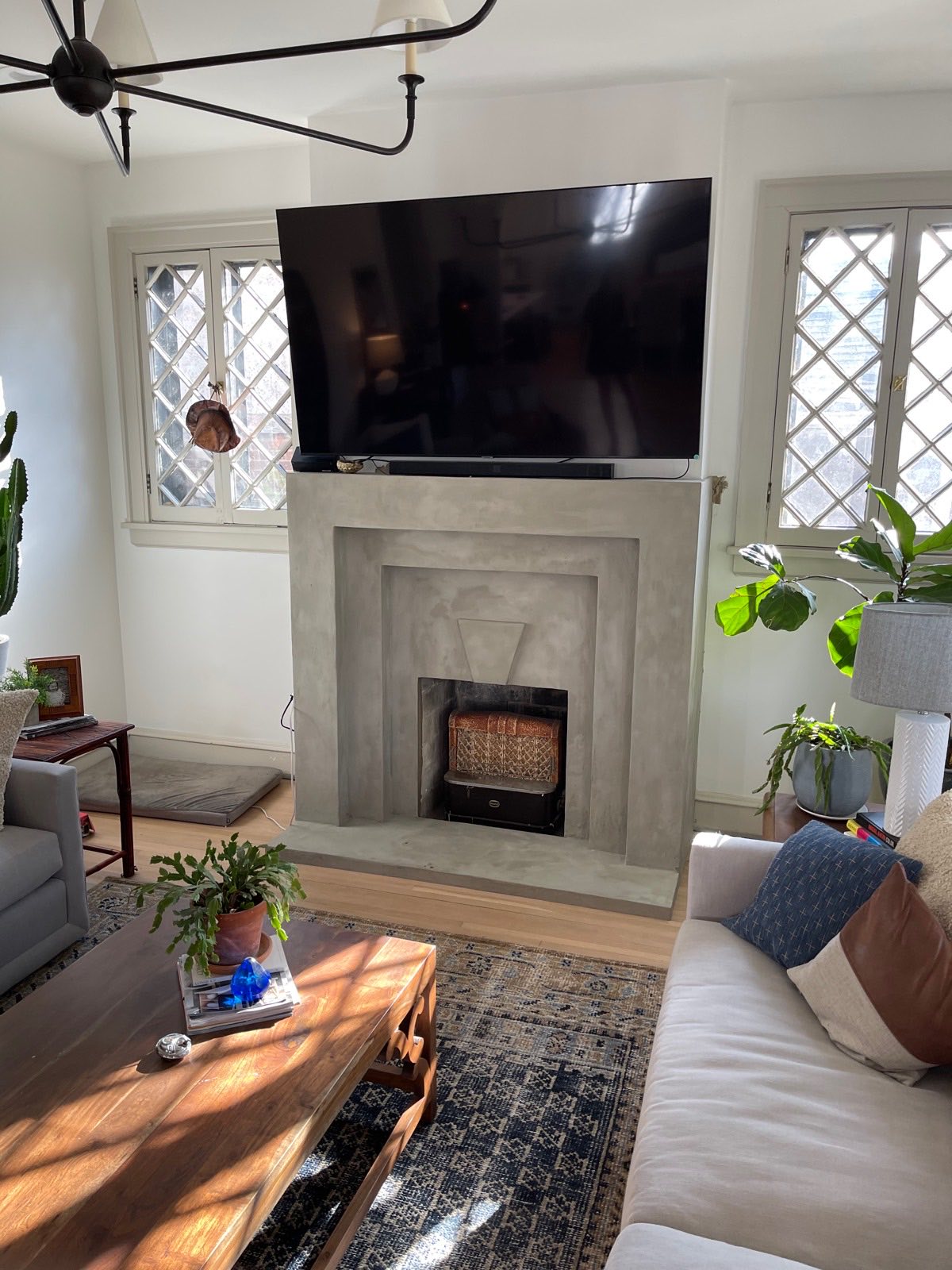 Velluto microcement fireplace surround in a 1920s East Nashville living room, the original cast-iron coal basket kept in place between leaded diamond-pane windows